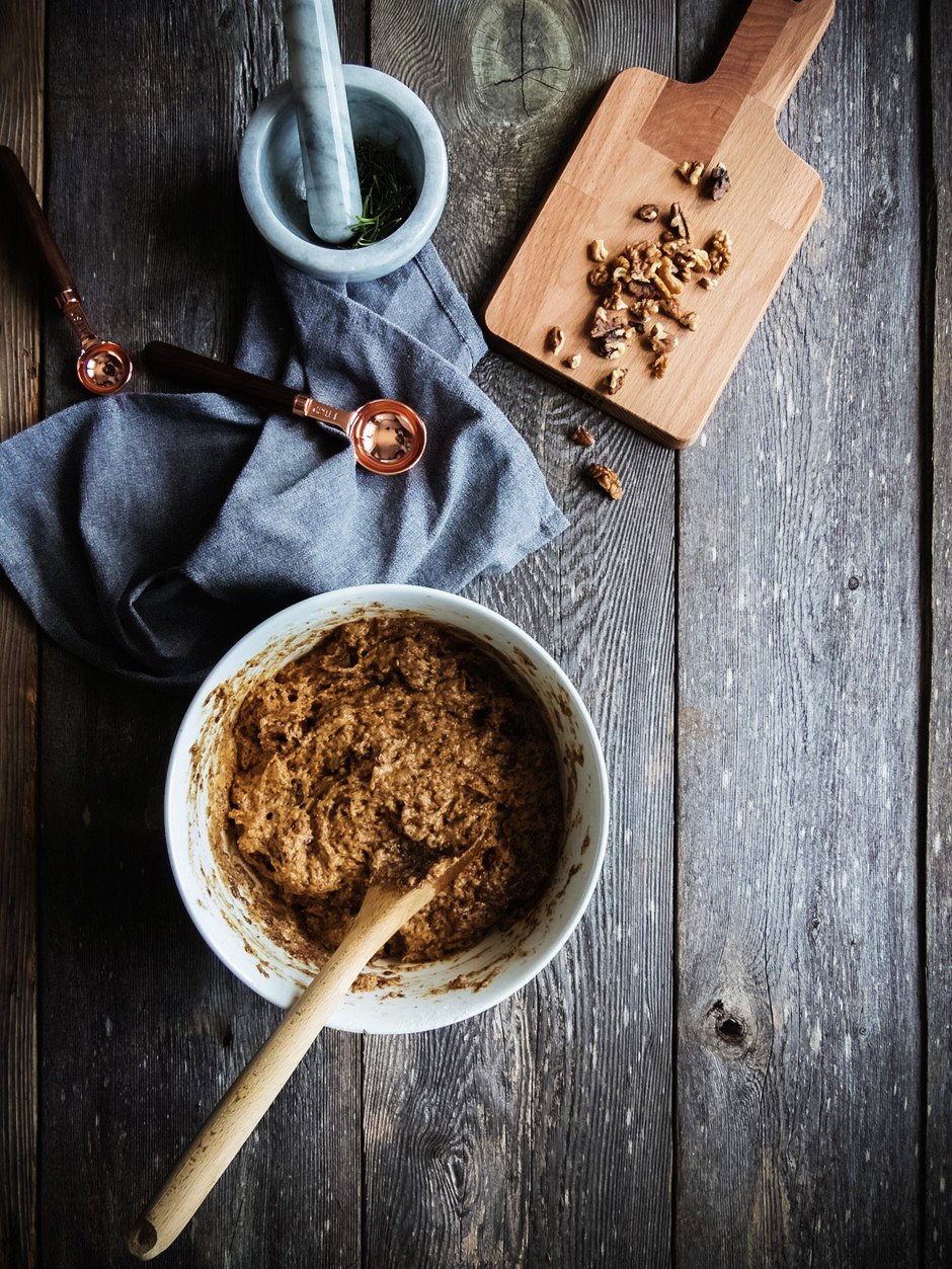 date nut bread batter in a bowl with measuring spoons and chopped walnuts on a cutting board.
