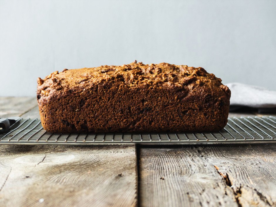 a portrait of a side view of a rosemary bread loaf on a wire rack on a wood surface.