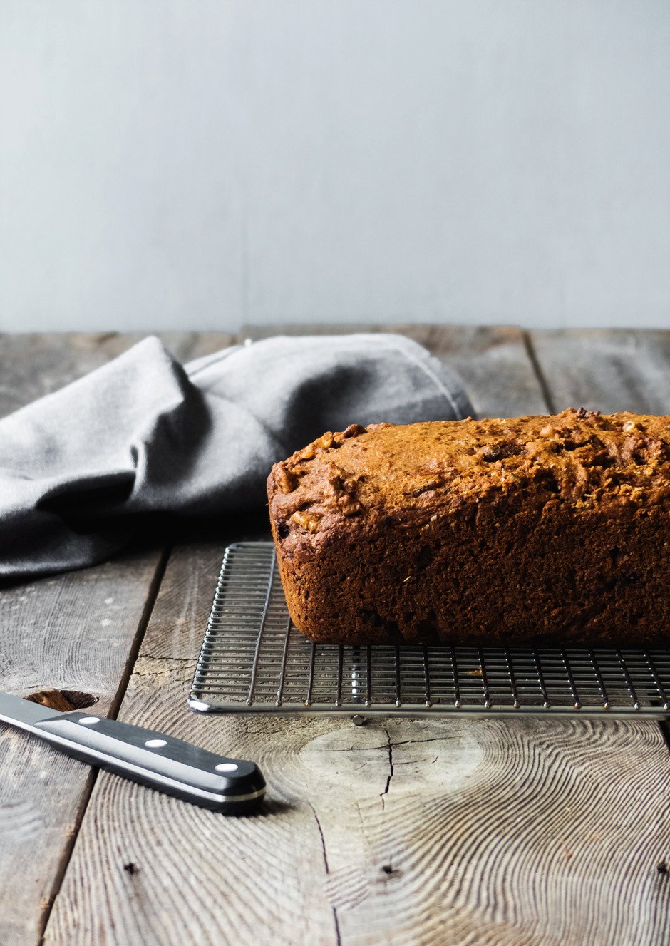 a portrait of rosemary bread loaf on a wire rack on a wood surface with a blue linen and knife.