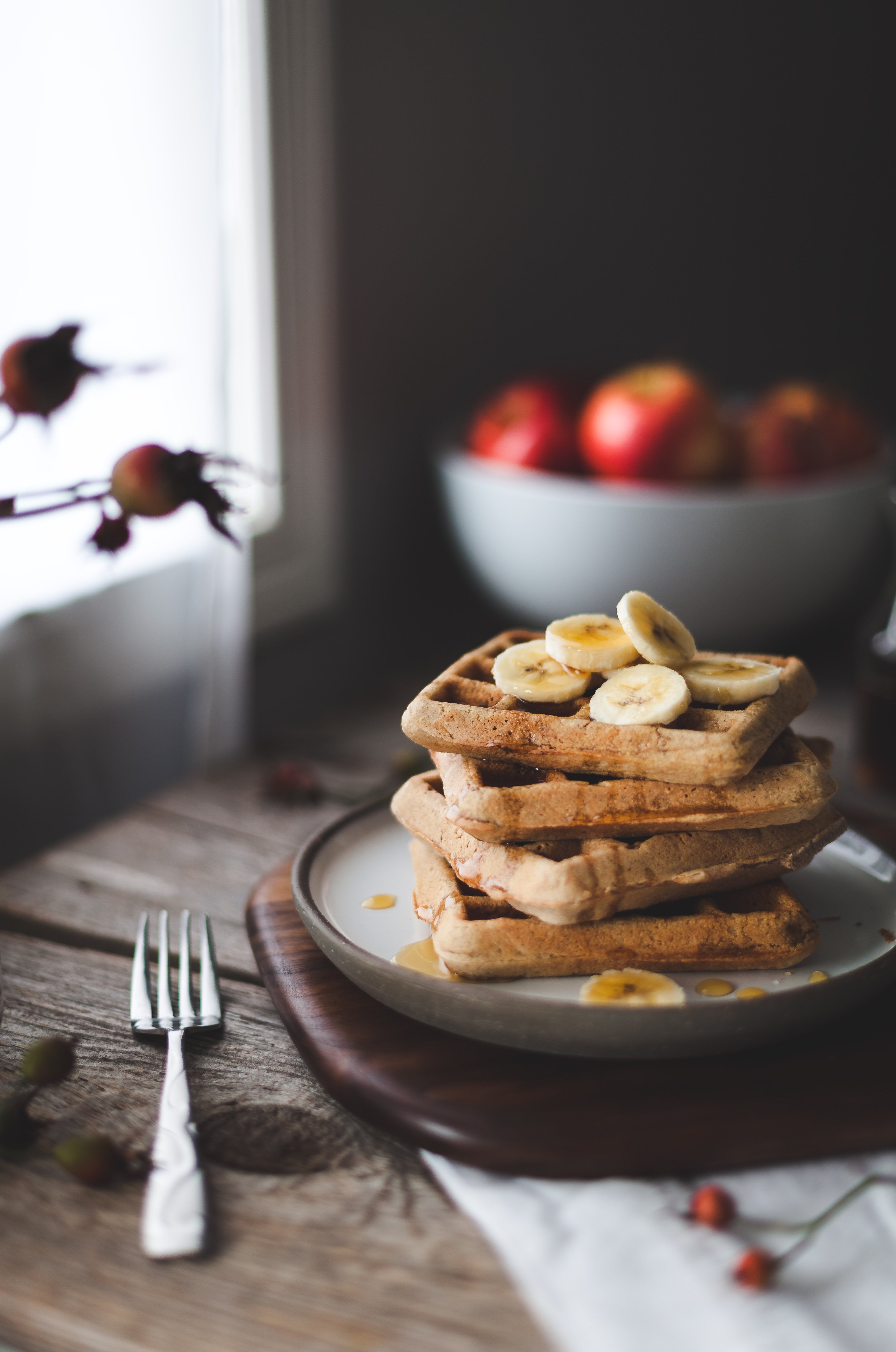 a stack of a waffles with banana slices on top sitting next to a window.