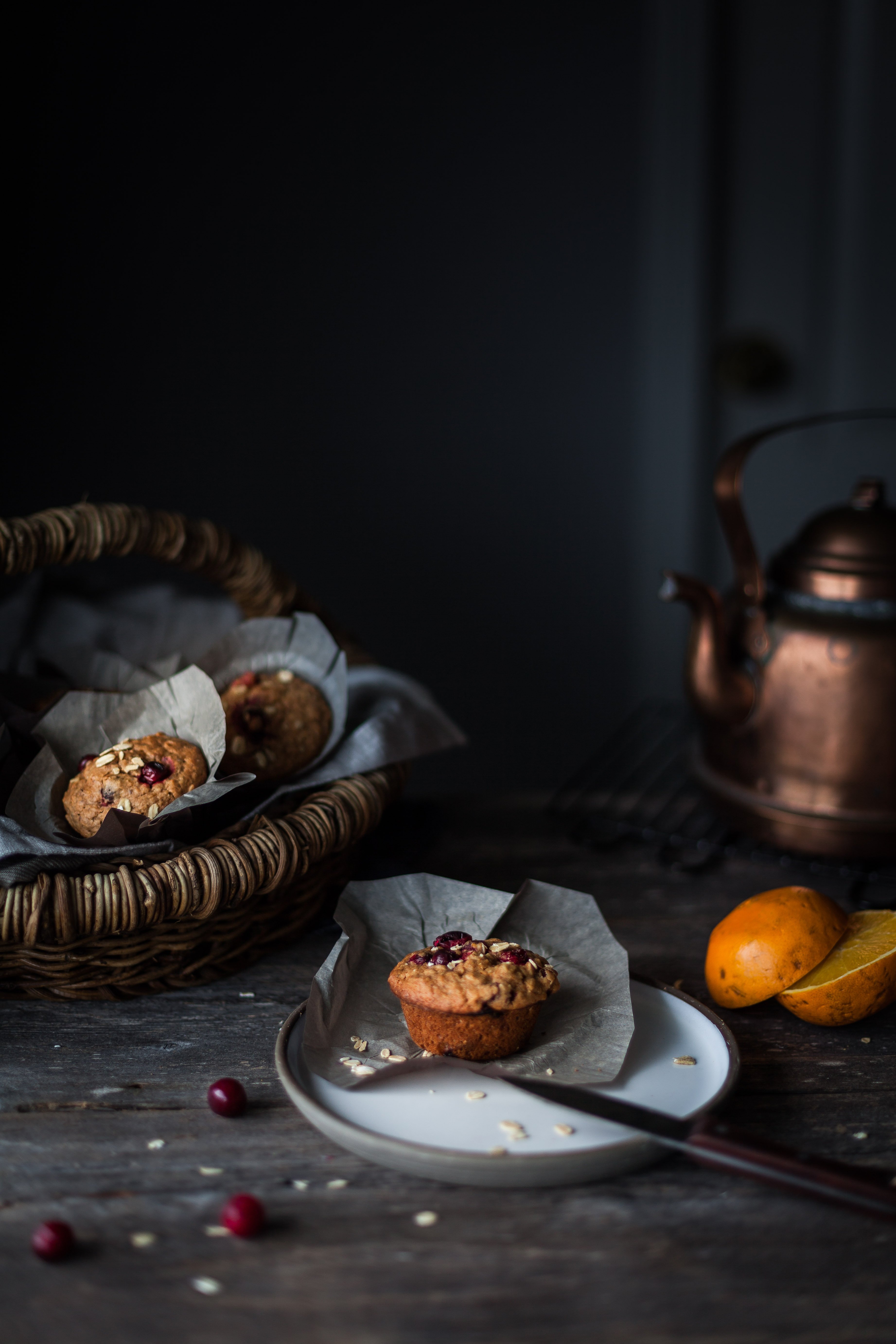 A head on image of a muffin on a plate with a basket of muffins and copper kettle in the background.