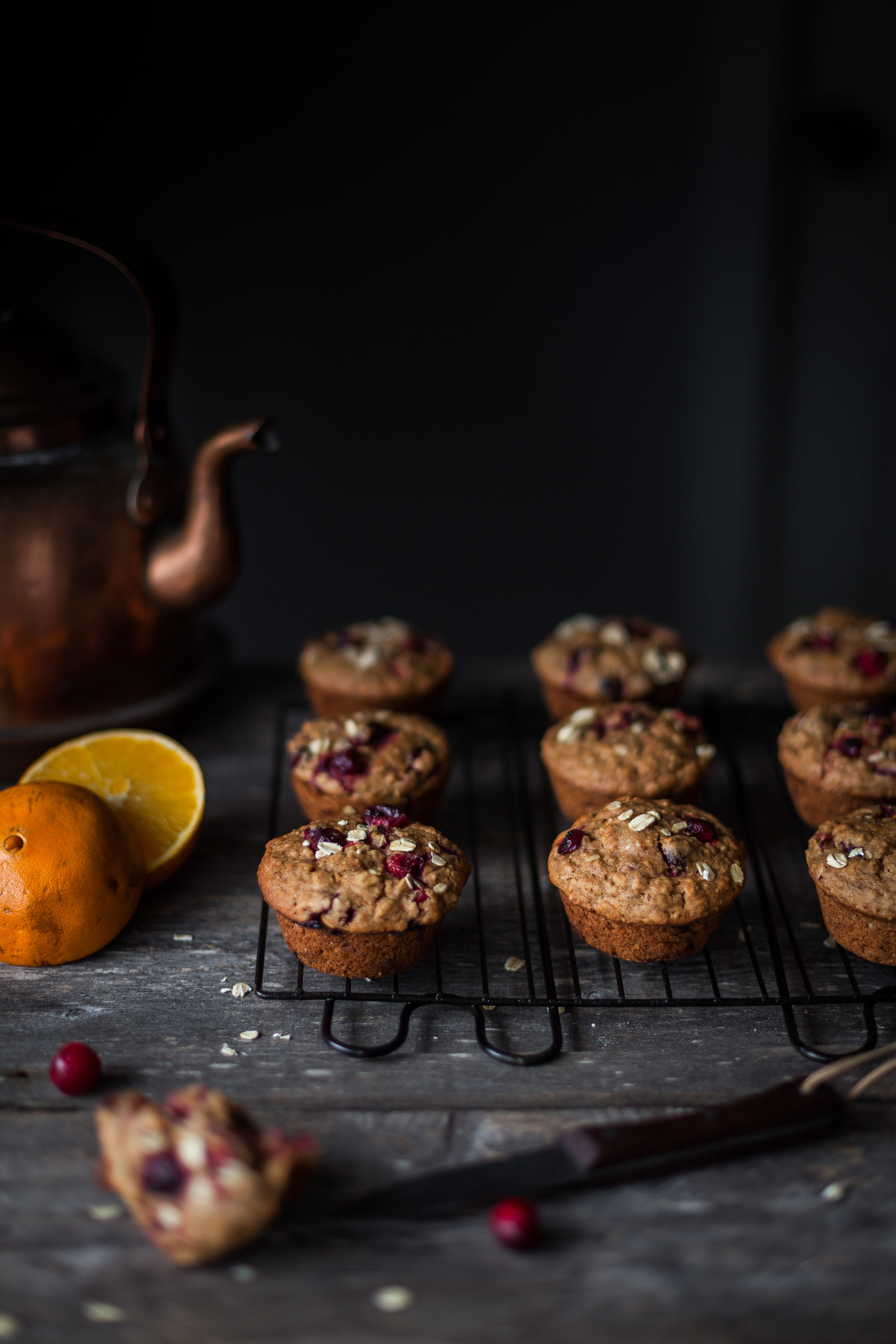 a head on image of vegan cranberry orange muffins sitting on a cooling rack with a copper kettle in the background.