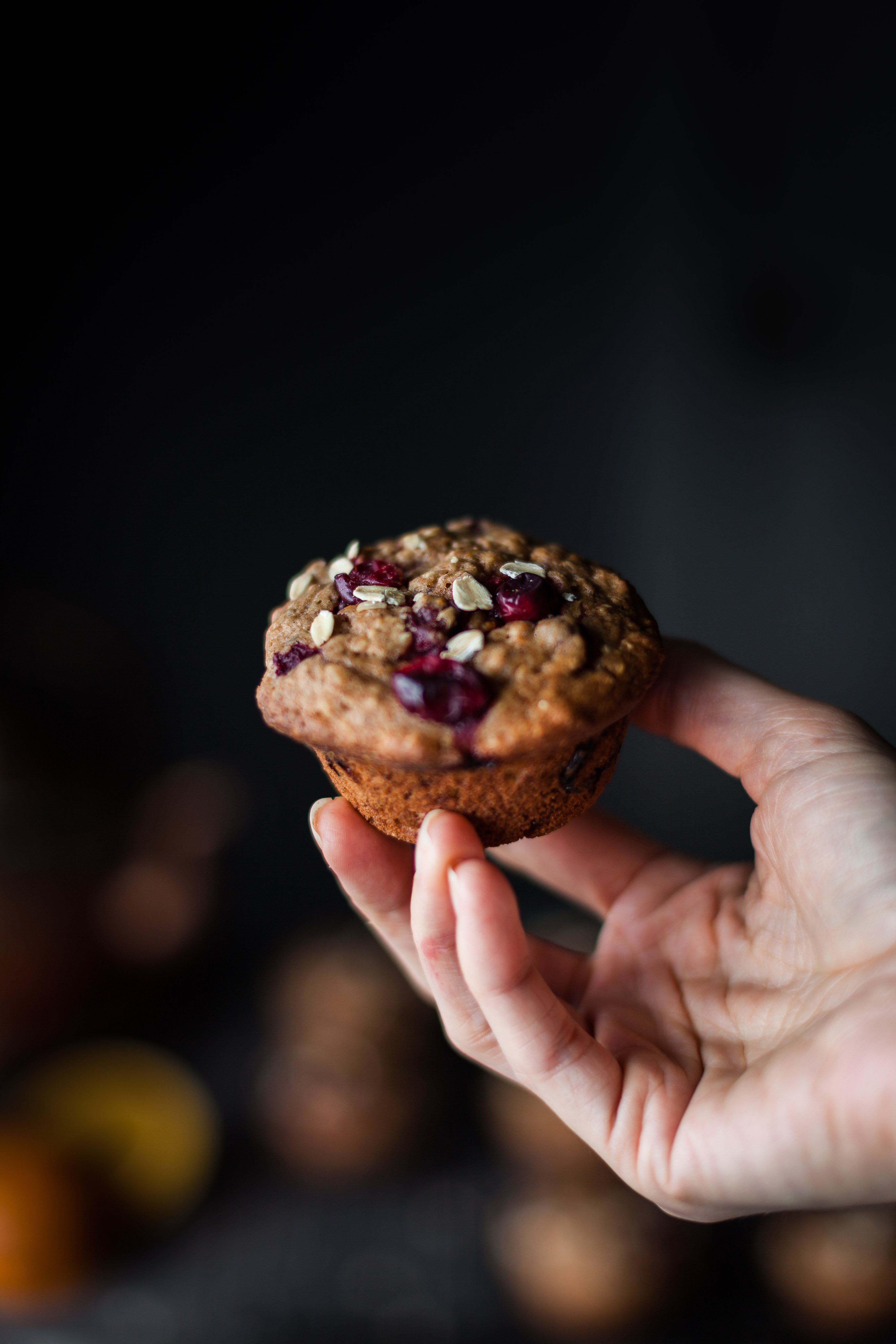 a hand holding a vegan cranberry orange muffin with oats.