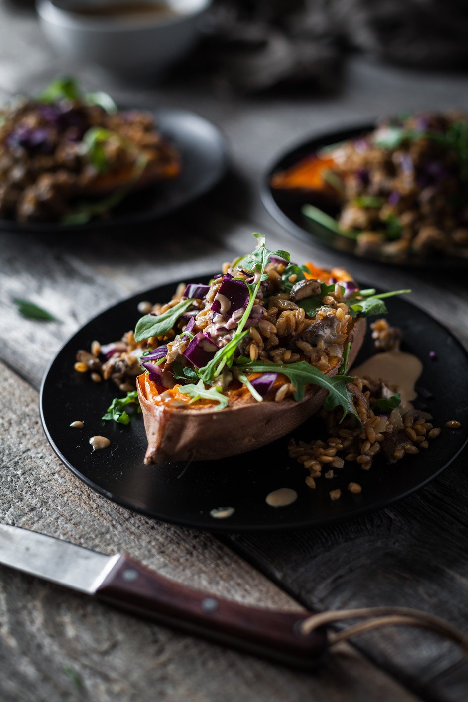 side view of a stuffed sweet potato on a black plate with a knife.