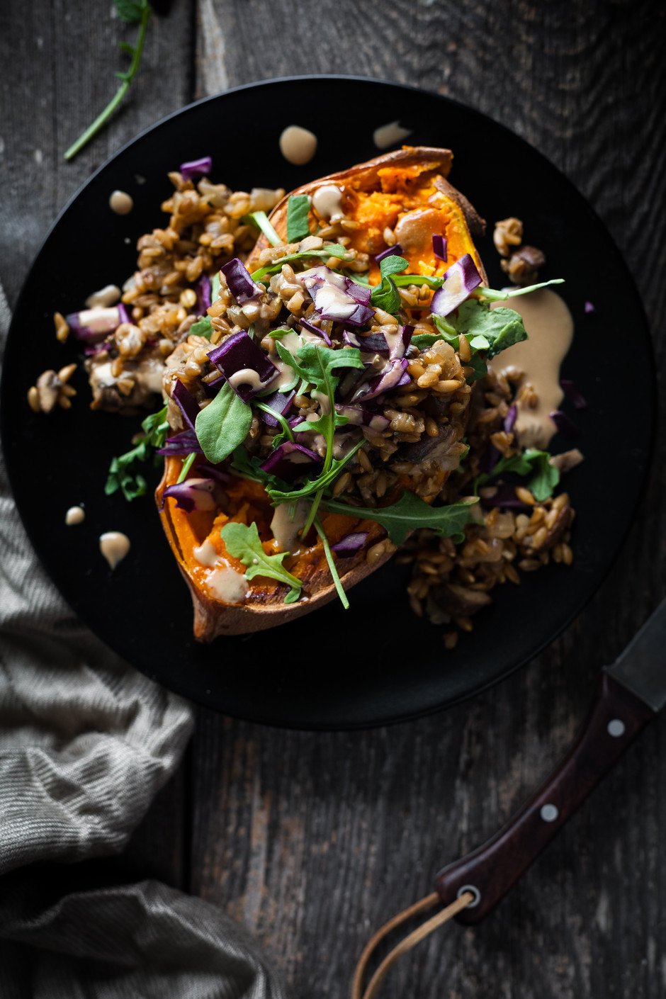 closeup overhead of a stuffed sweet potato on a black plate with rosemary.