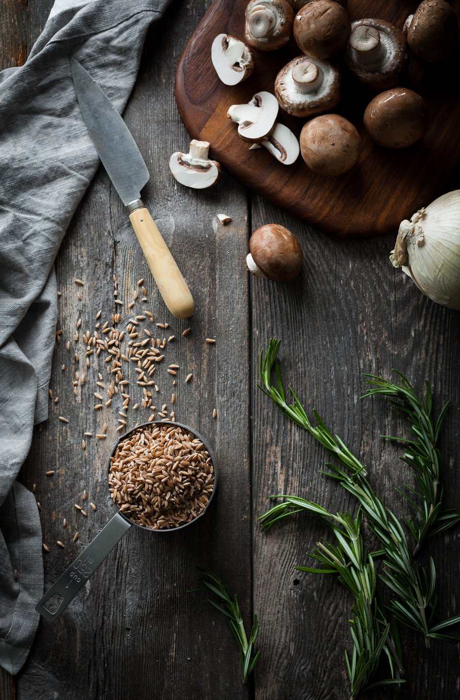 overhead of mushrooms ona cutting board with farro, rosemary and onions.