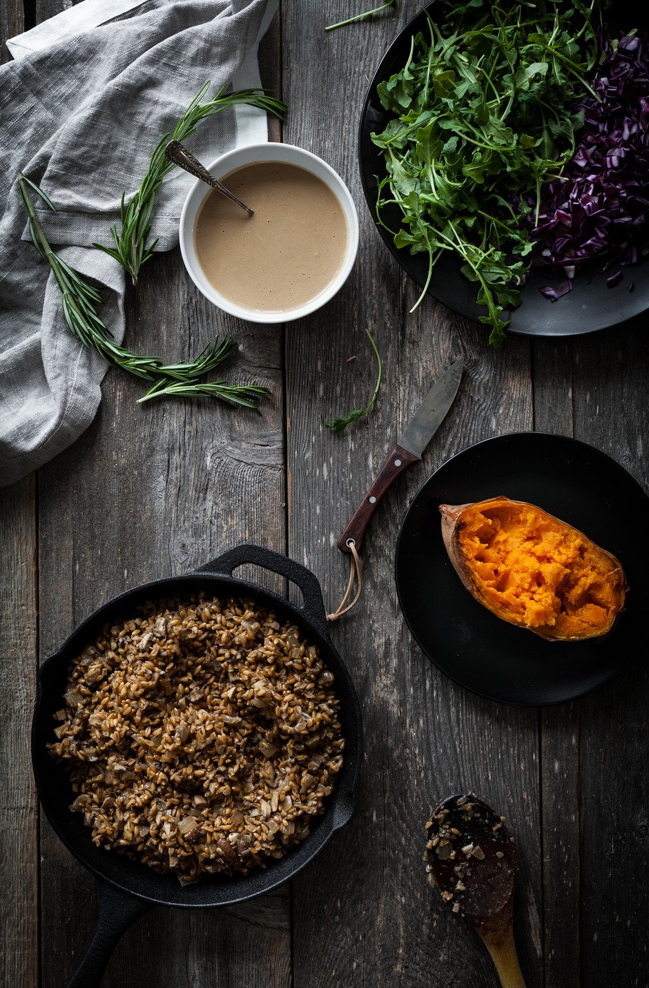 overhead of farro in a pan, a baked sweet potato, dressing, and fresh vegetables.