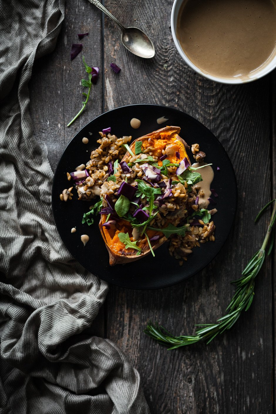 overhead of a stuffed sweet potato on a black plate with rosemary.