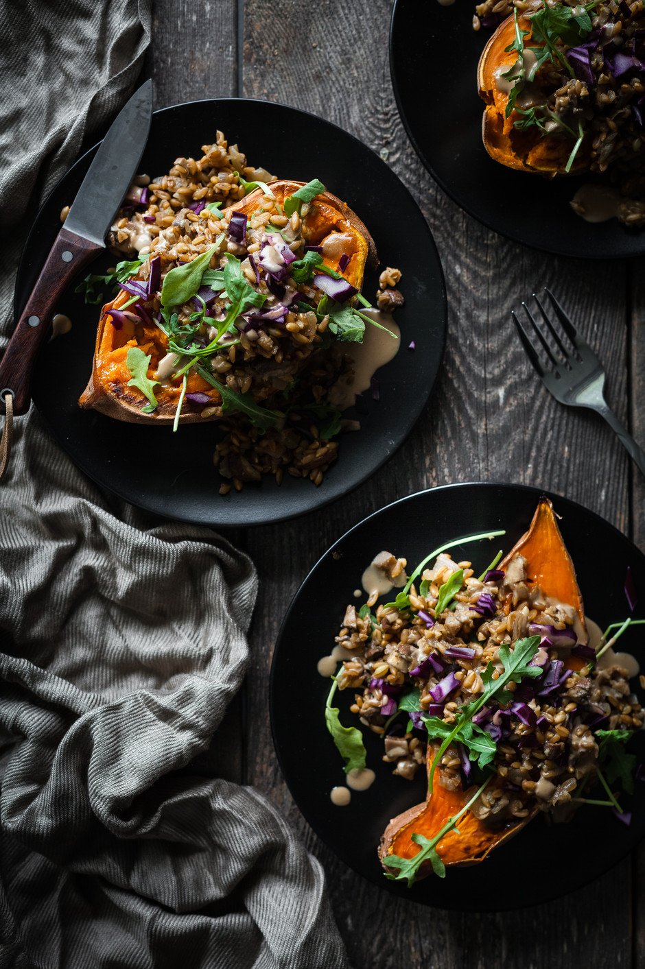 overhead of two stuffed sweet potatoes on a black plates with a linen and knife.