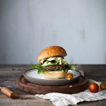 a veggies burger on a white plate and cutting board with cherry tomatoes