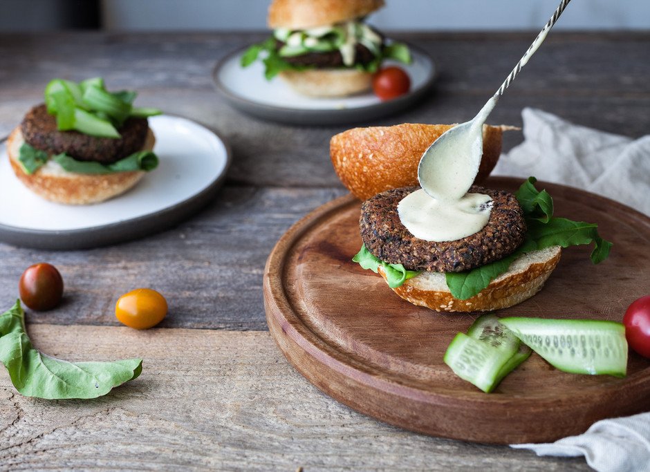 a spoon spreading sauce on a burger on a cutting board with two burgers in the background.