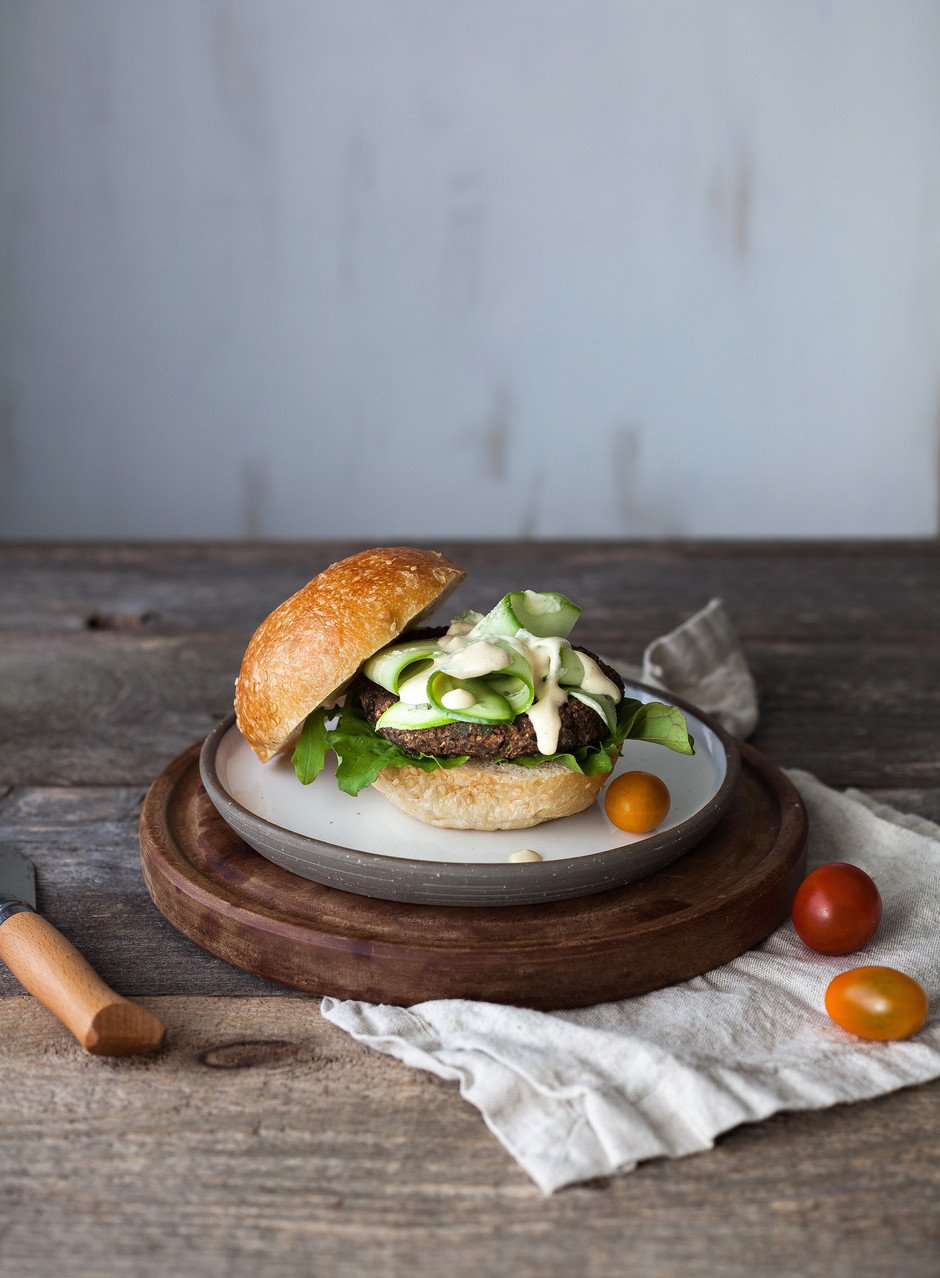 portrait of a dressed veggie burger with the top bun placed on the side and tomatoes on the plate.