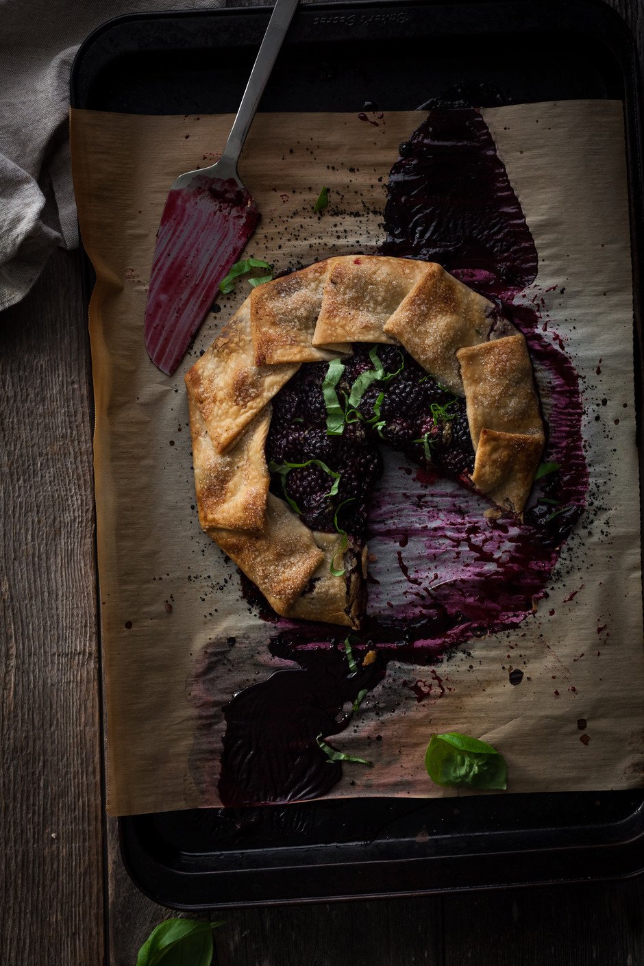 overhead of a blackberry galette on a baking tray with a slice missing and a cake server.