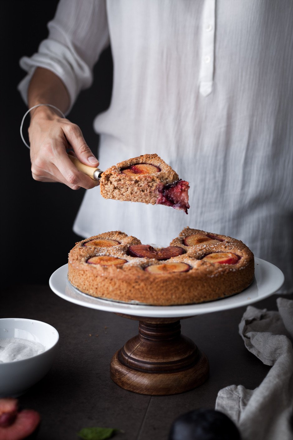 a person holding a cake slice on a knife with a cake beneath it.