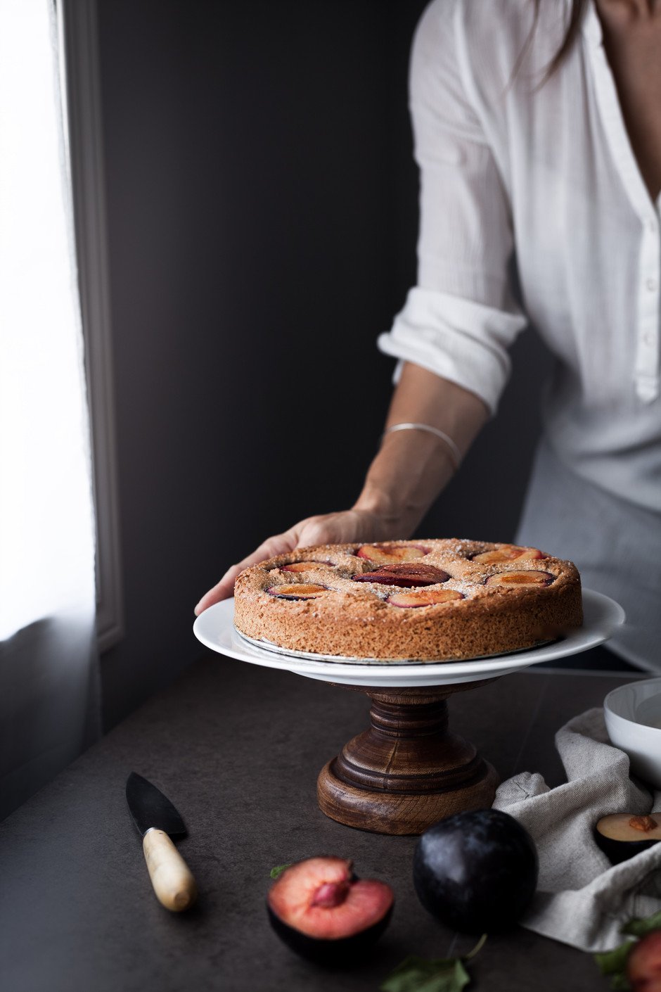 portrait of a person holding a plum cake on a cake stand.