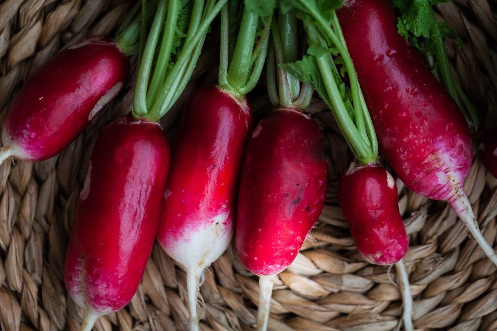 overhead closeup image of 6 fresh radishes in a basket.