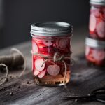 a head on image of a jar of pickled radishes with a twine bow.
