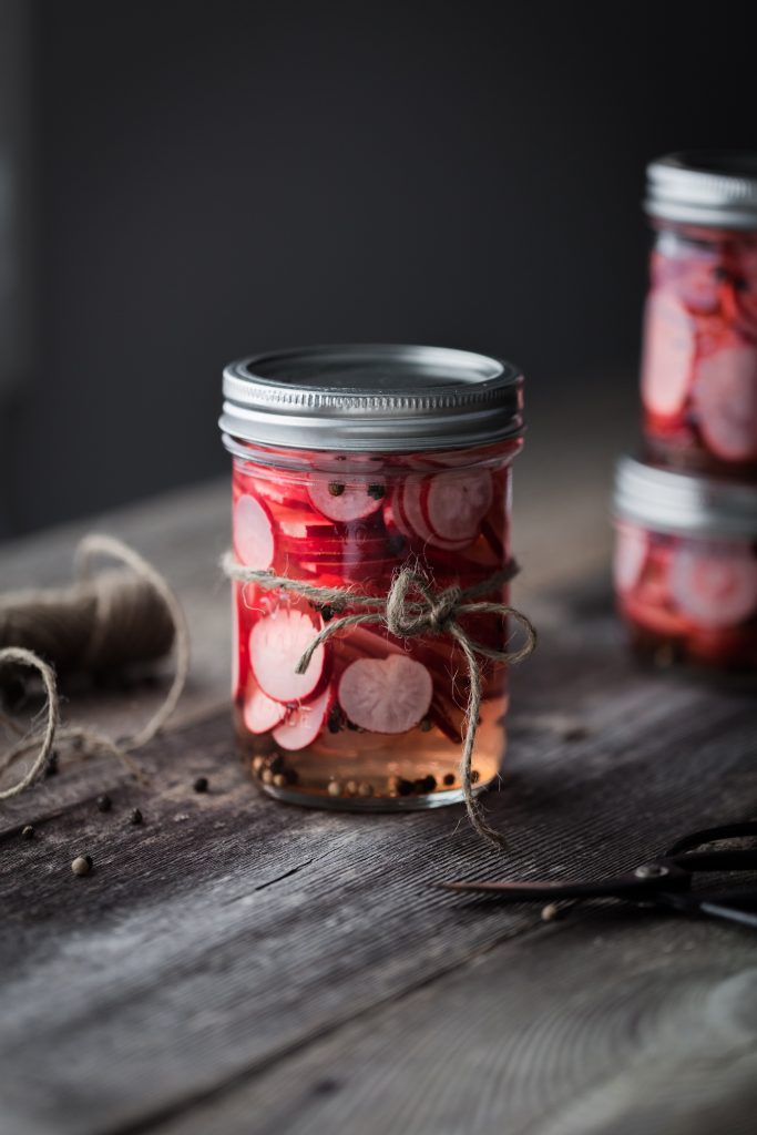 a portrait of pickled radishes in a jar on a wood surface.