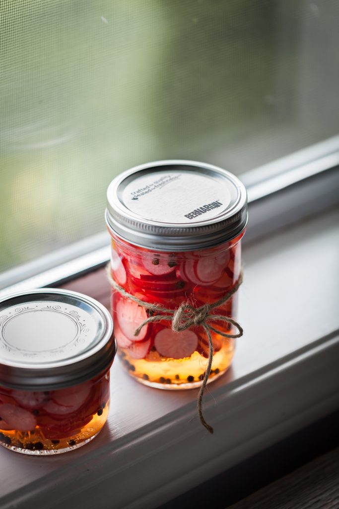 a portrait of jar of pickled radishes sitting on a window sill.