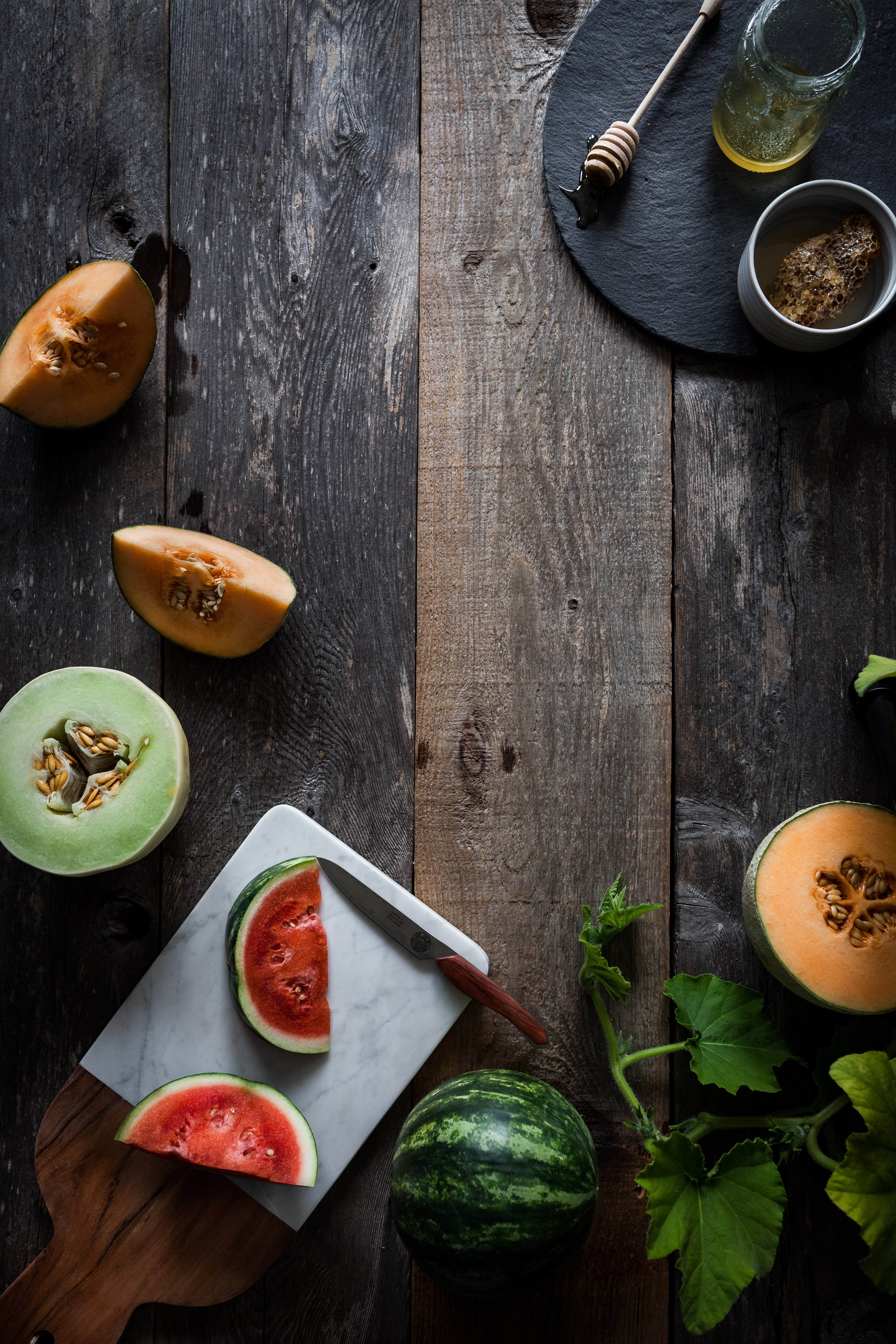 overhead view of honeycomb, fresh cut melons and vines on a wood surface.