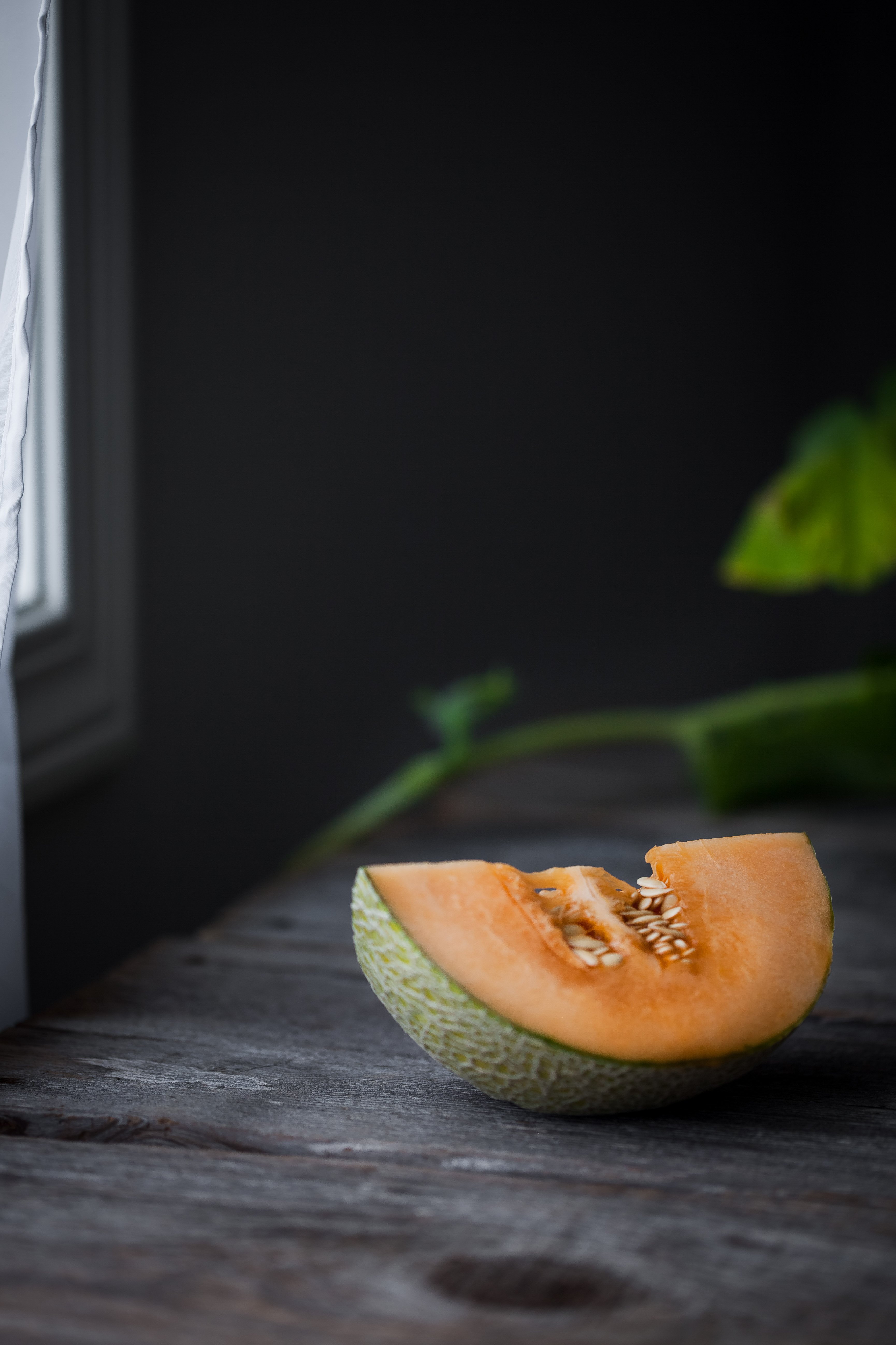 portrait view of a quartered cantaloupe melon on a table with vines in the background.