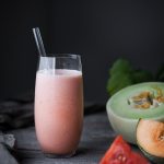 Portrait view of a pink melon smoothie with slices of fresh melon on the side.