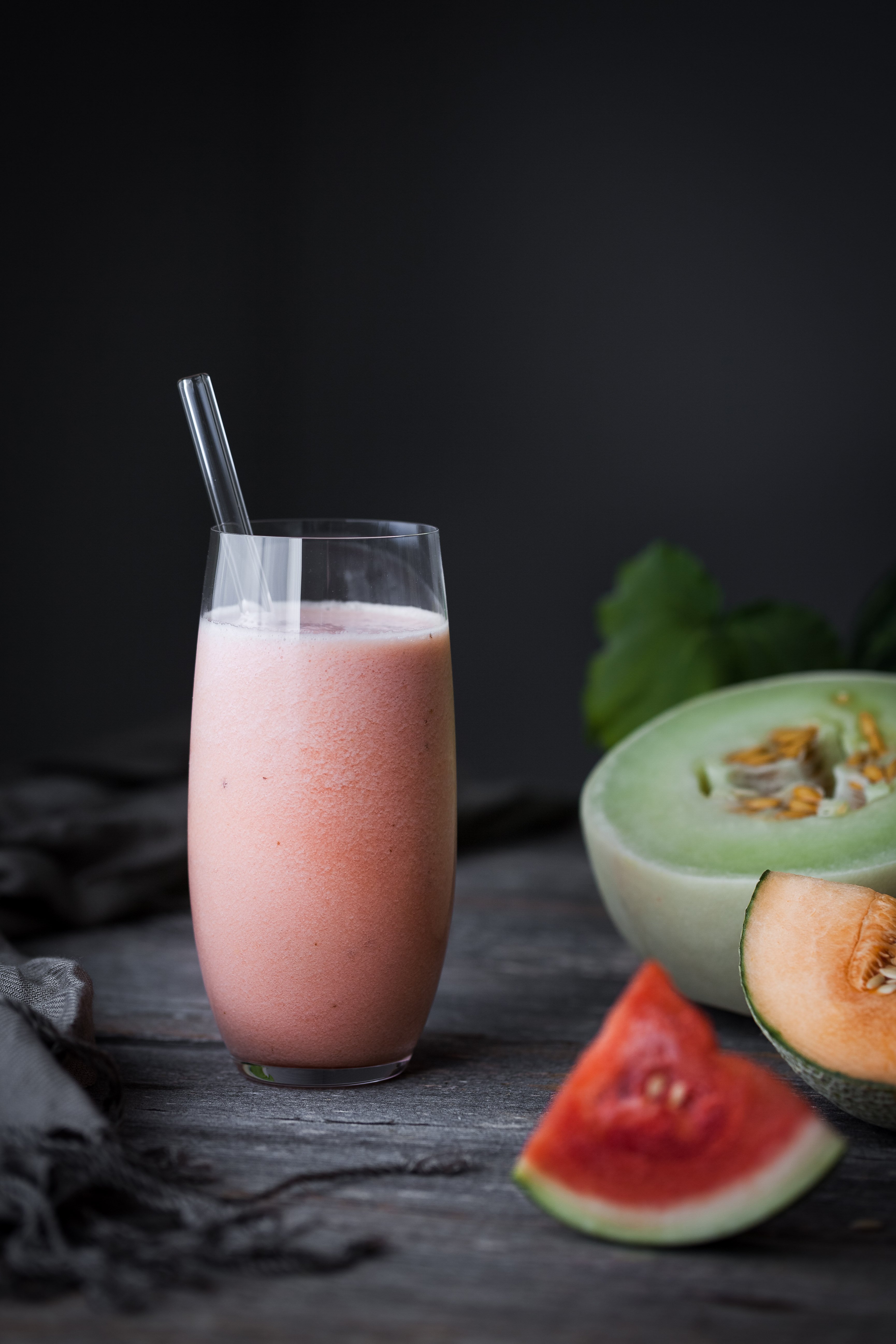 portrait view of a melon smoothie with a straw next to fresh melons. 