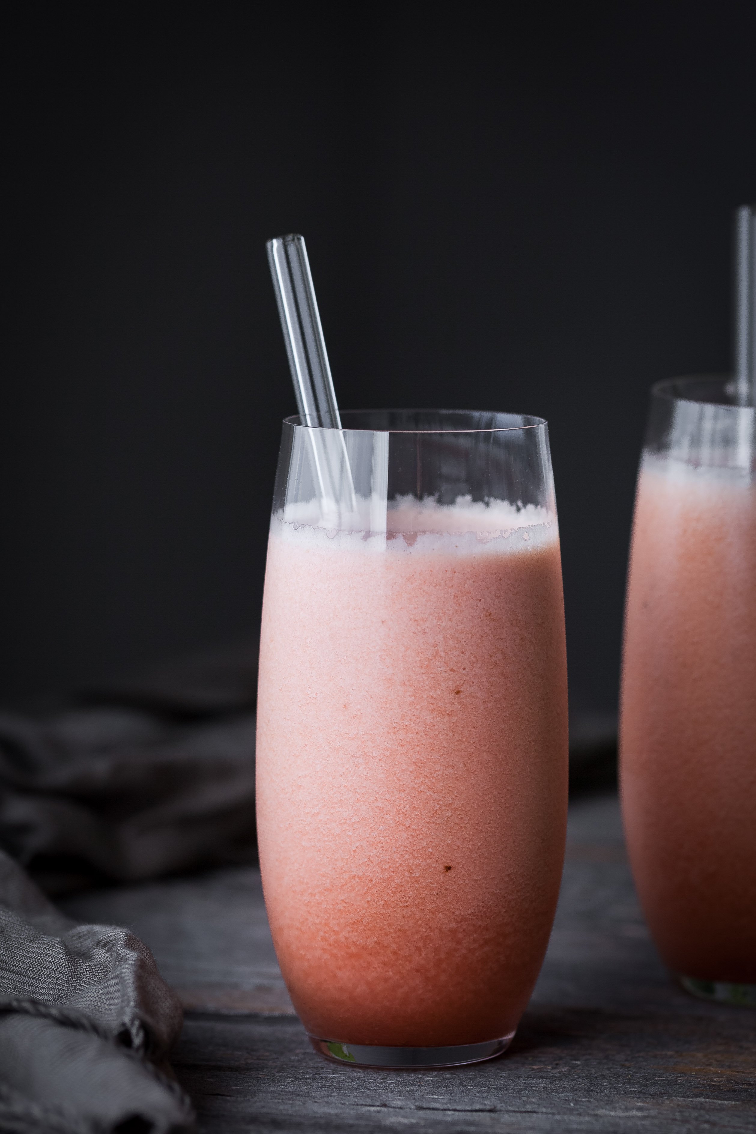 portrait view of two glasses of melon smoothie with glass straws.