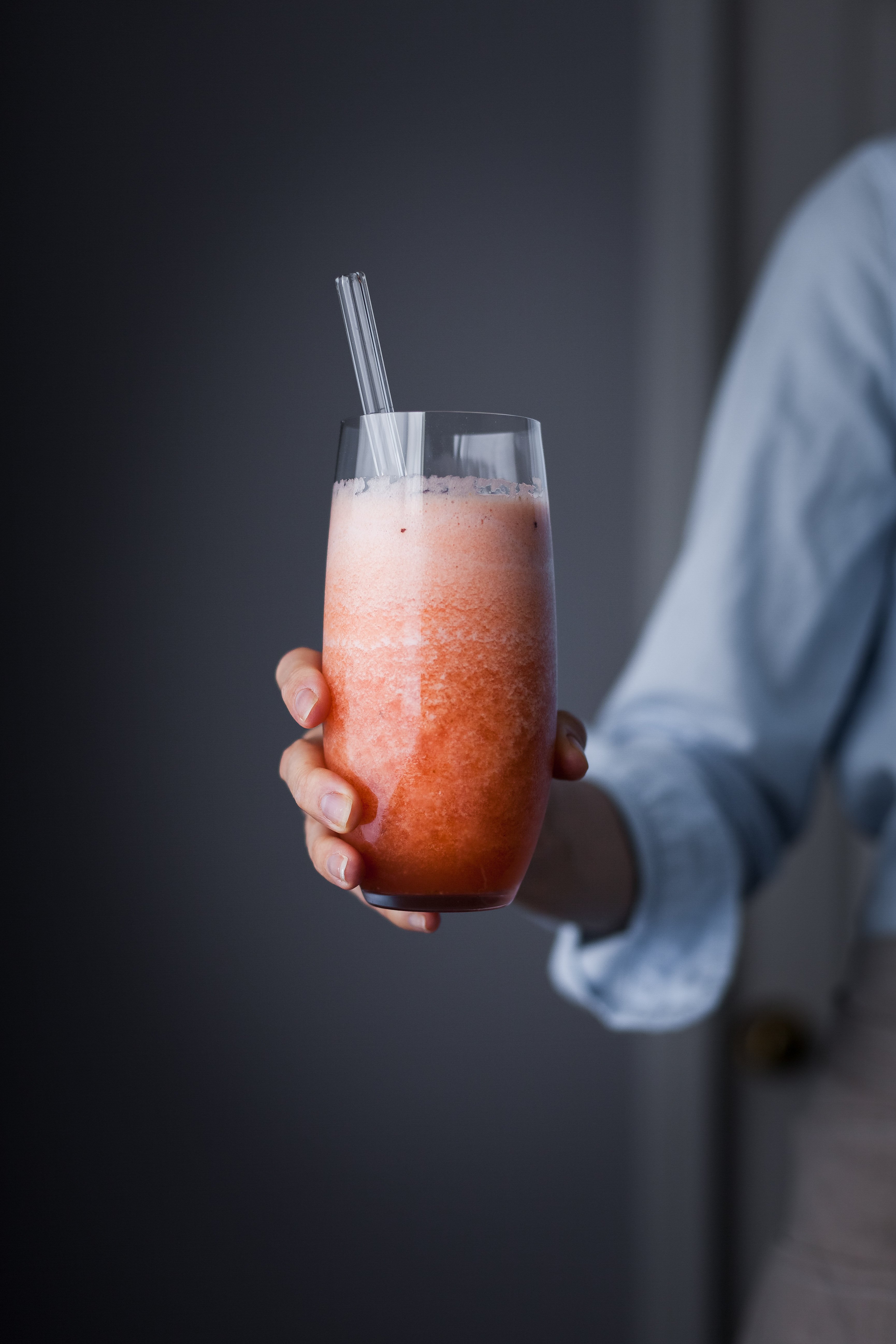 a person holding a glass of triple melon smoothie with a straw in it.