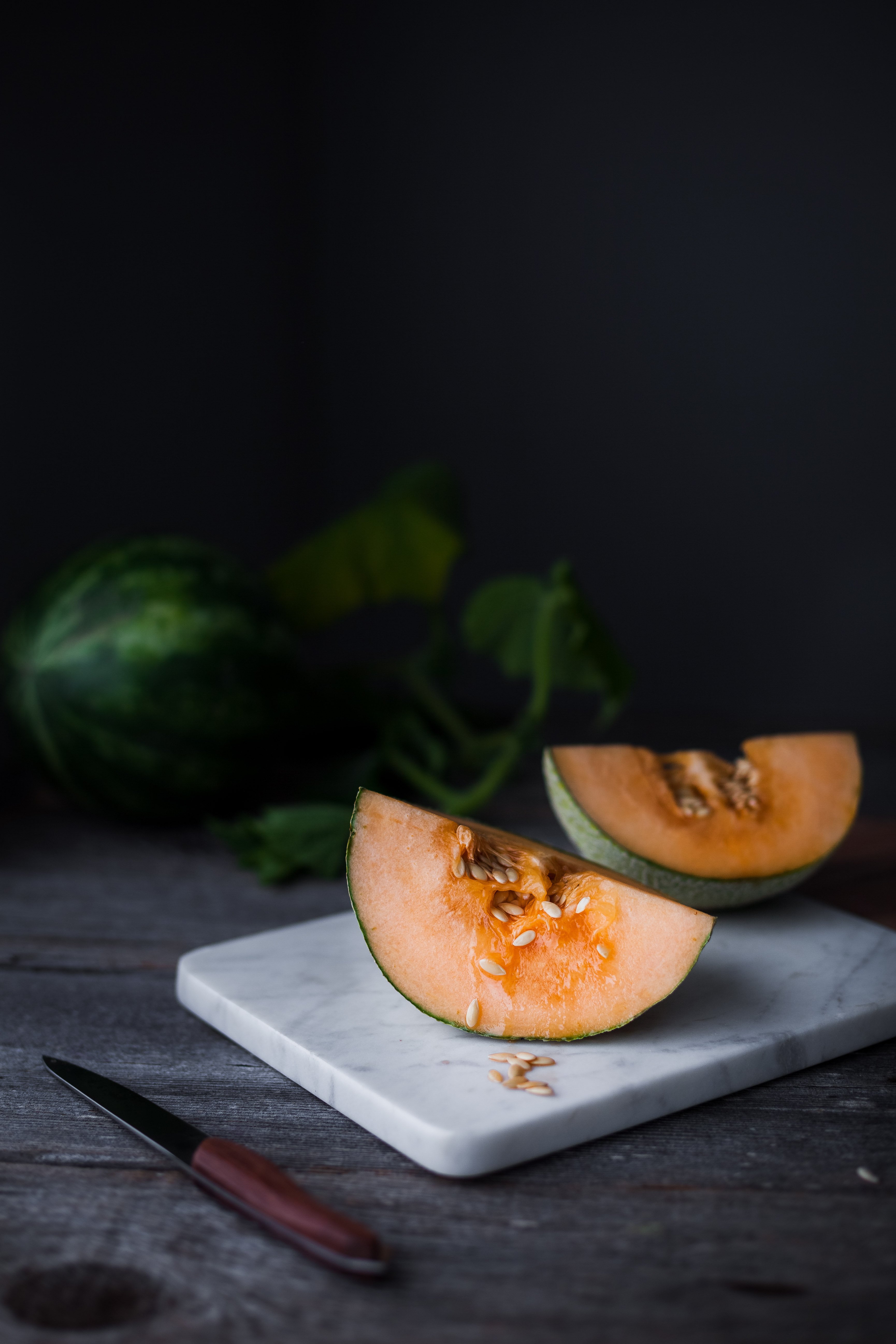 portrait view of a sliced cantaloupe on a cutting board.