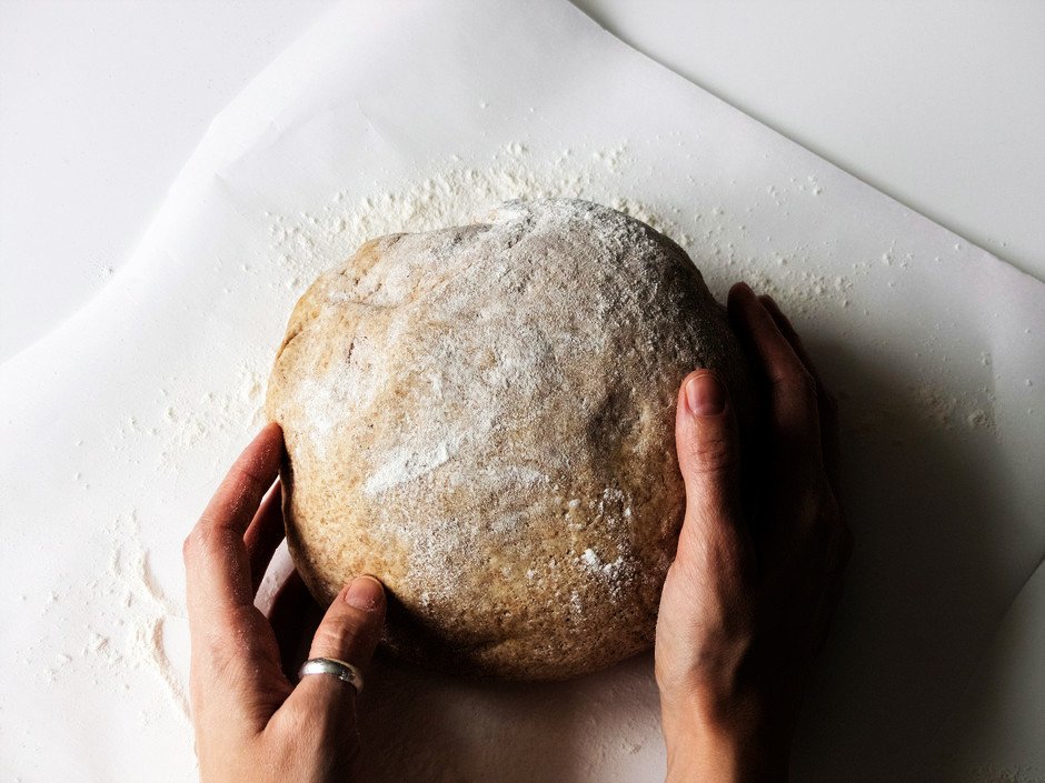 overhead image of a bread dough ball with two hands holding the ball.