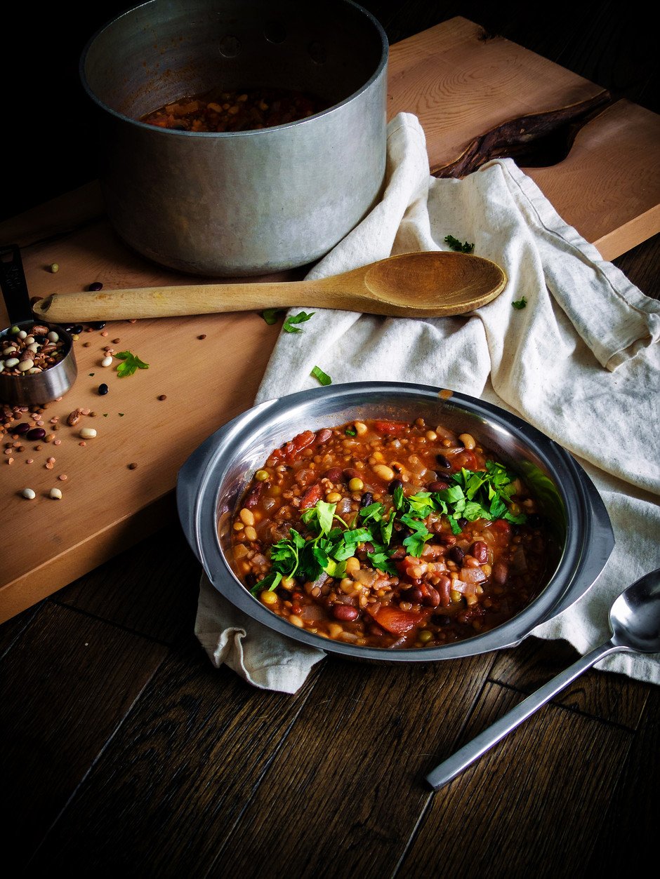 a bowl of bean soup with a wooden spoon, linen, and pot.