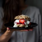 a person holding a strawberry shortcake on a black plate.