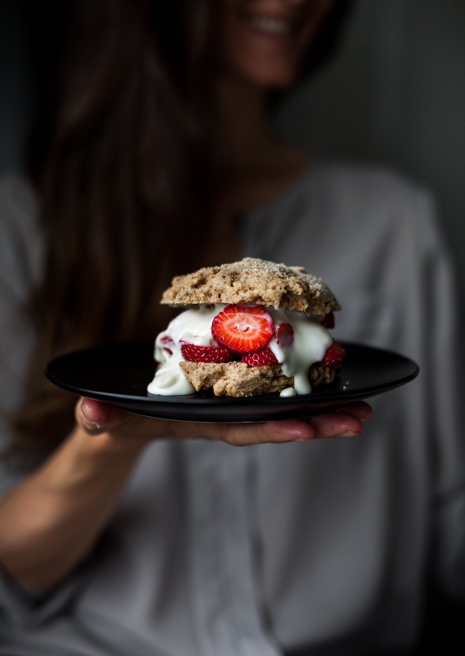 a person holding a strawberry shortcake on a black plate.