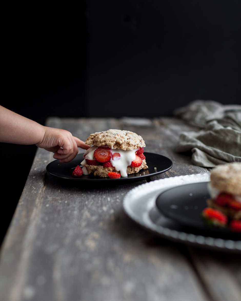 portrait view of a child's hand picking at a strawberry shortcake.