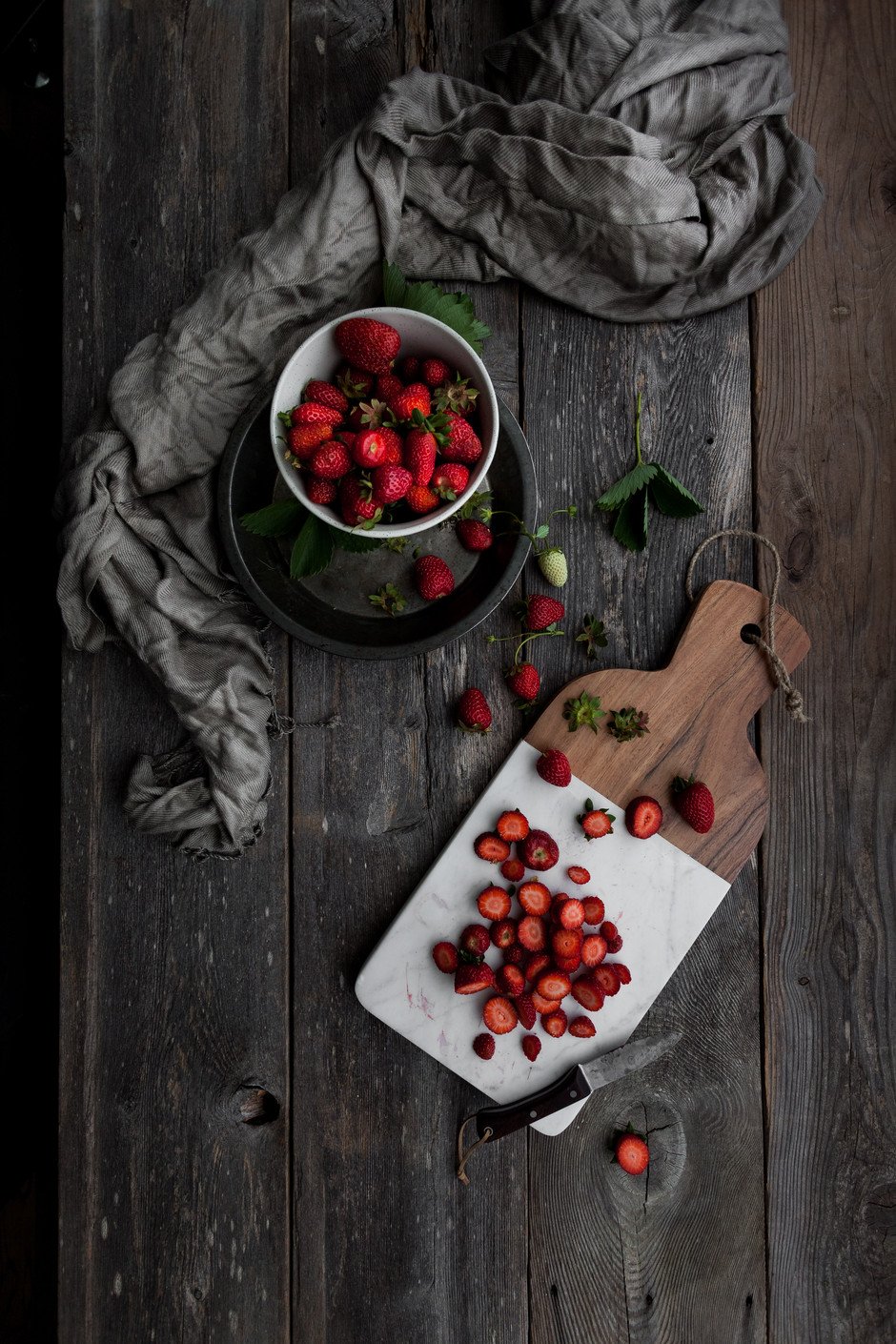 overhead view of slices strawberries on a cutting board and a bowl of fresh strawberries on the side.