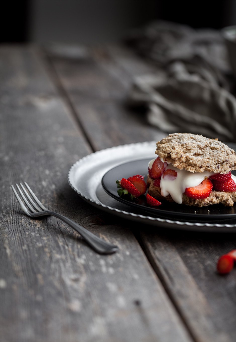 portrait view of a vegan strawberry shortcake on a black plate with a fork on a wood surface.