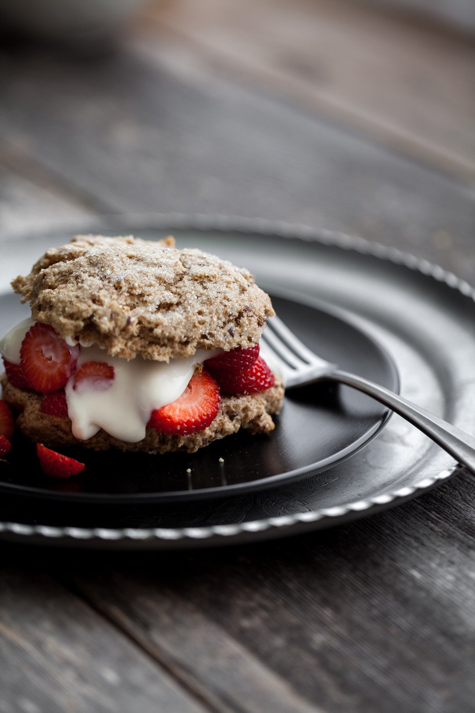 portrait view of a strawberry shortcake on a black plate with a fork.