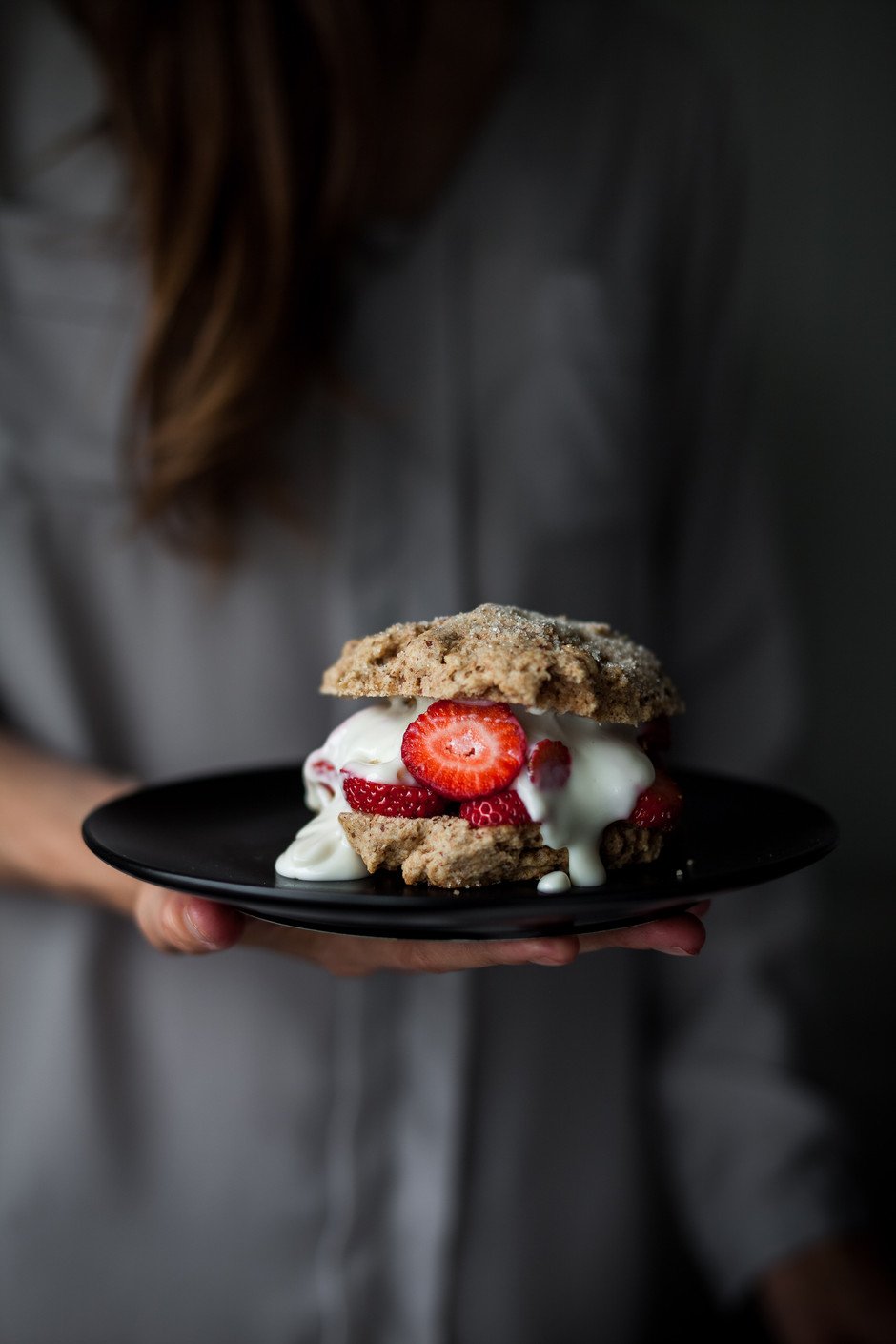 a person holding a vegan strawberry shortcake on a black plate.