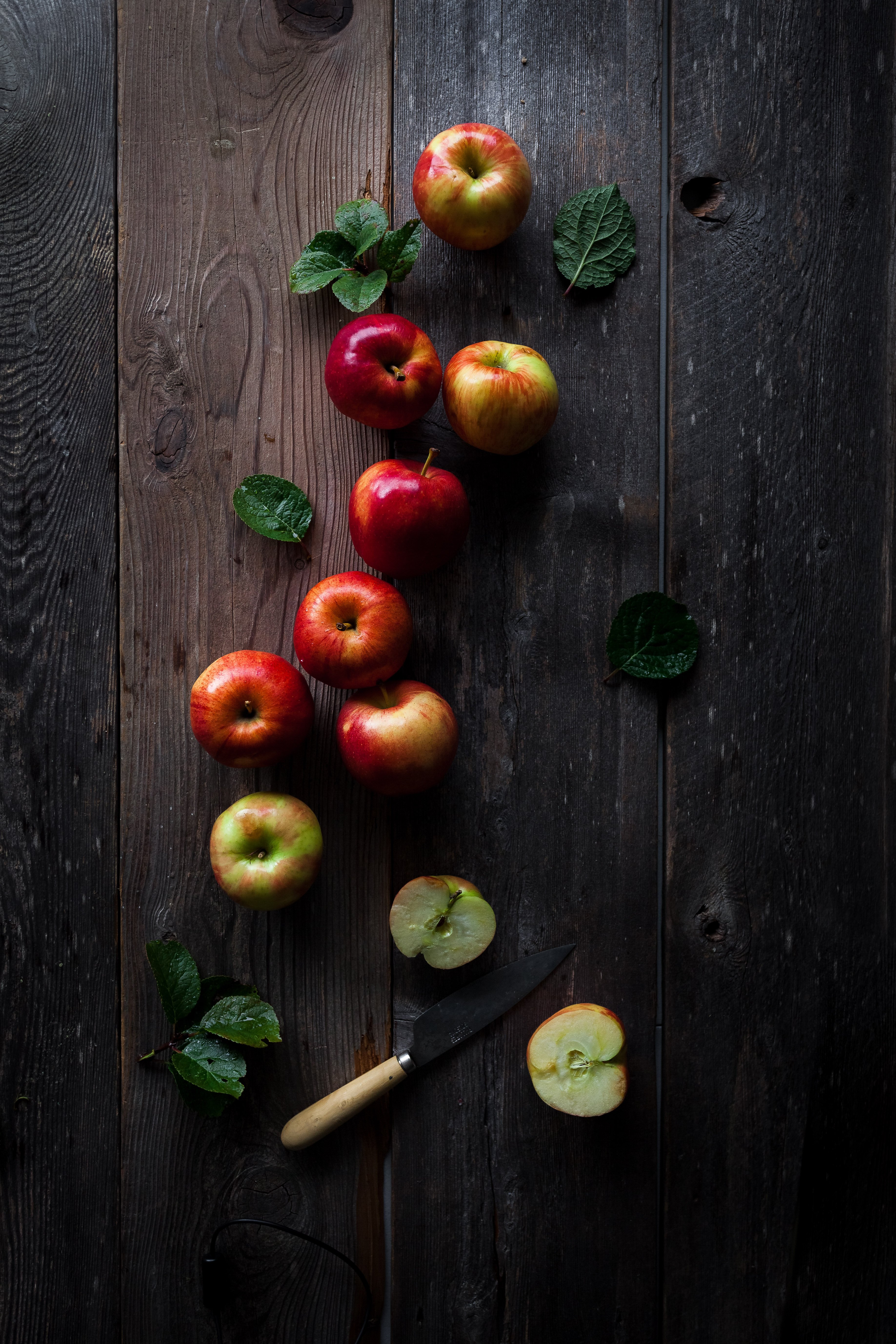 overhead image of red apples and leaves on a wooden surface with a knife at the bottom of the image.