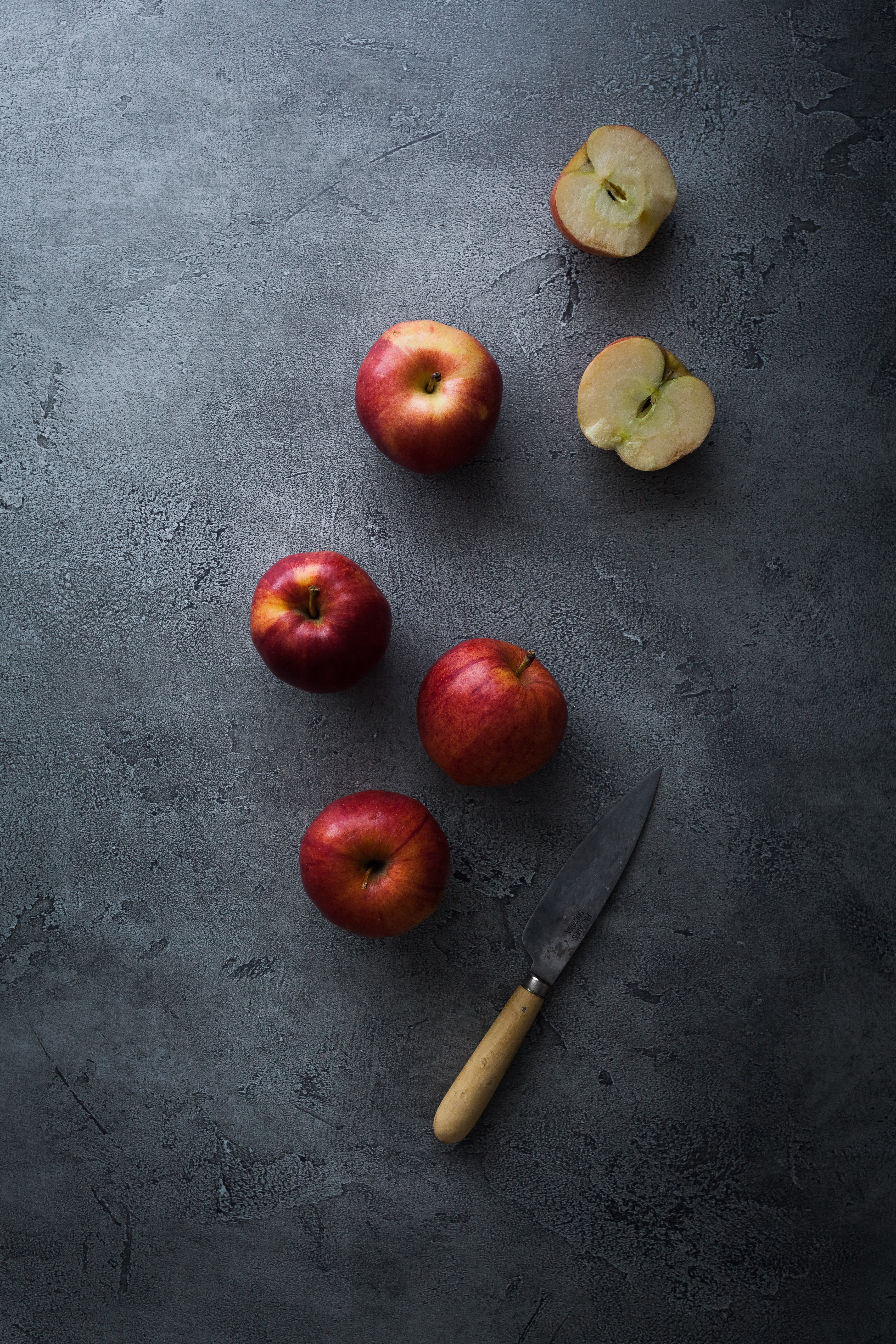 an overhead view of whole and sliced red apples on a grey stone surface with a paring knife.
