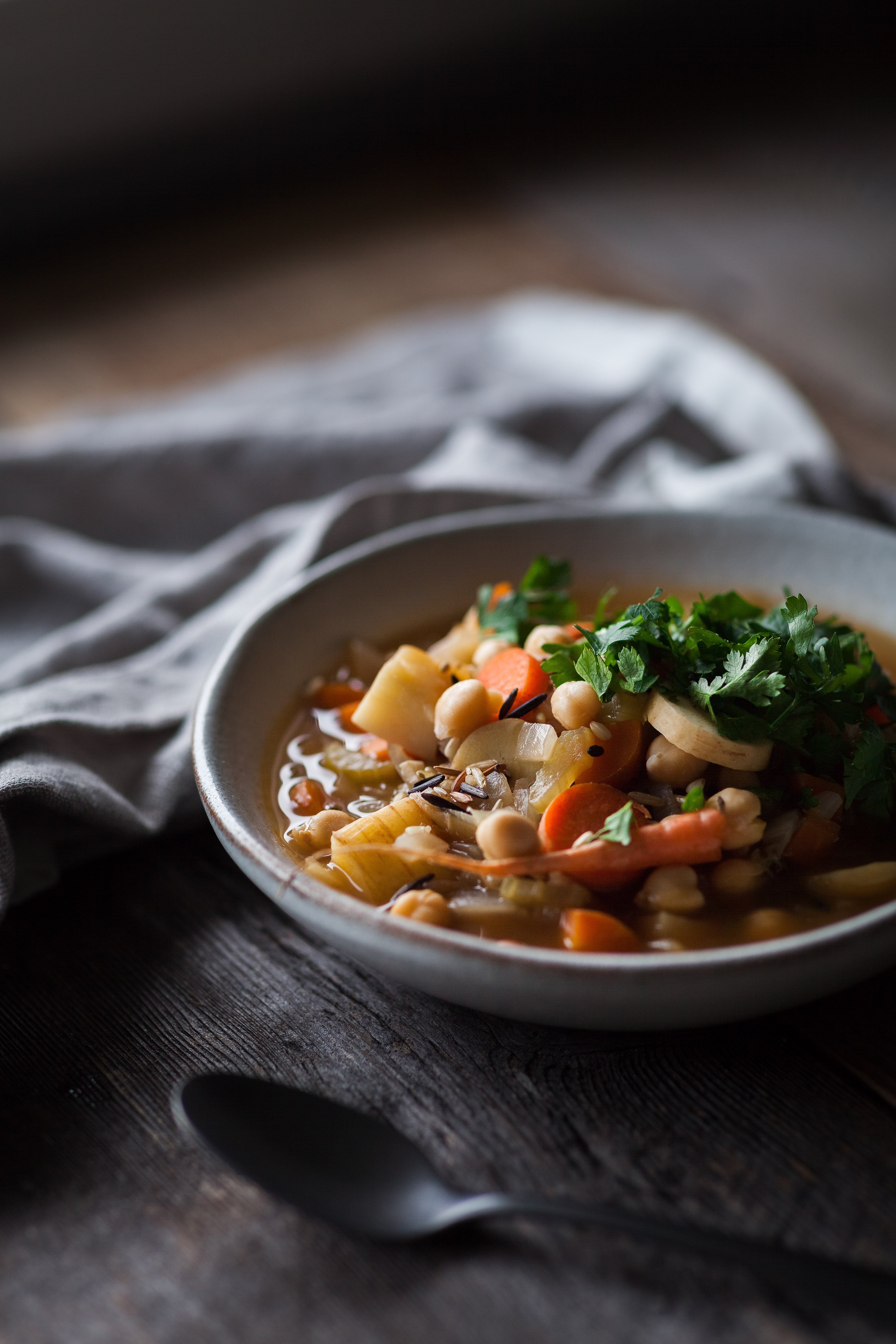 A ¾ angle image of a bowl of winter Vegetable Soup on a wooden surface with a white linen.