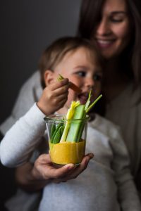 a head on image of a mom and toddler holding a jar of vegetables and golden dip.