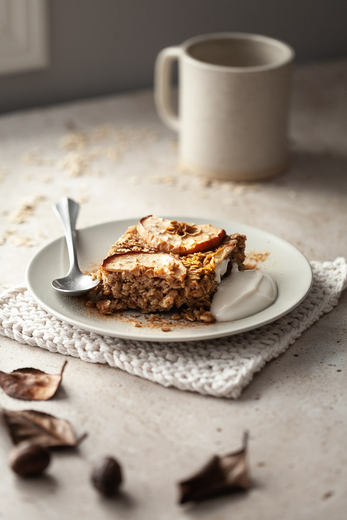 an angled close up of a plate of apple spice baked oatmeal with yogurt and a coffee mug in the background.