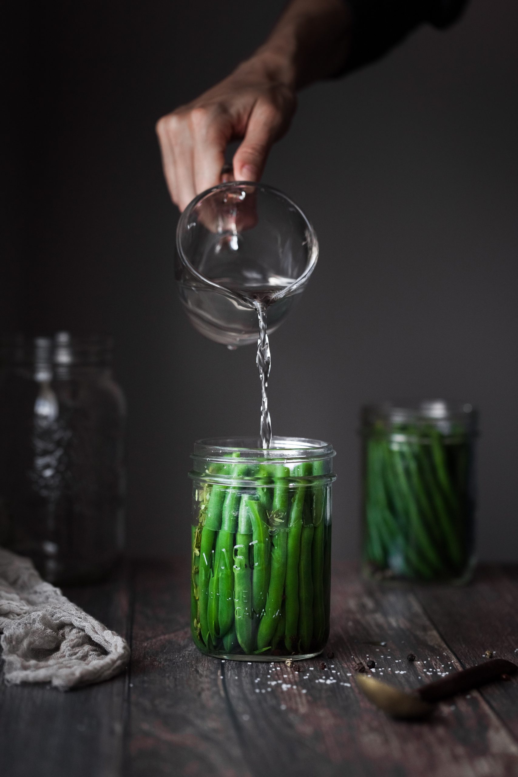 a person pouring brine into a jar filled with green beans.