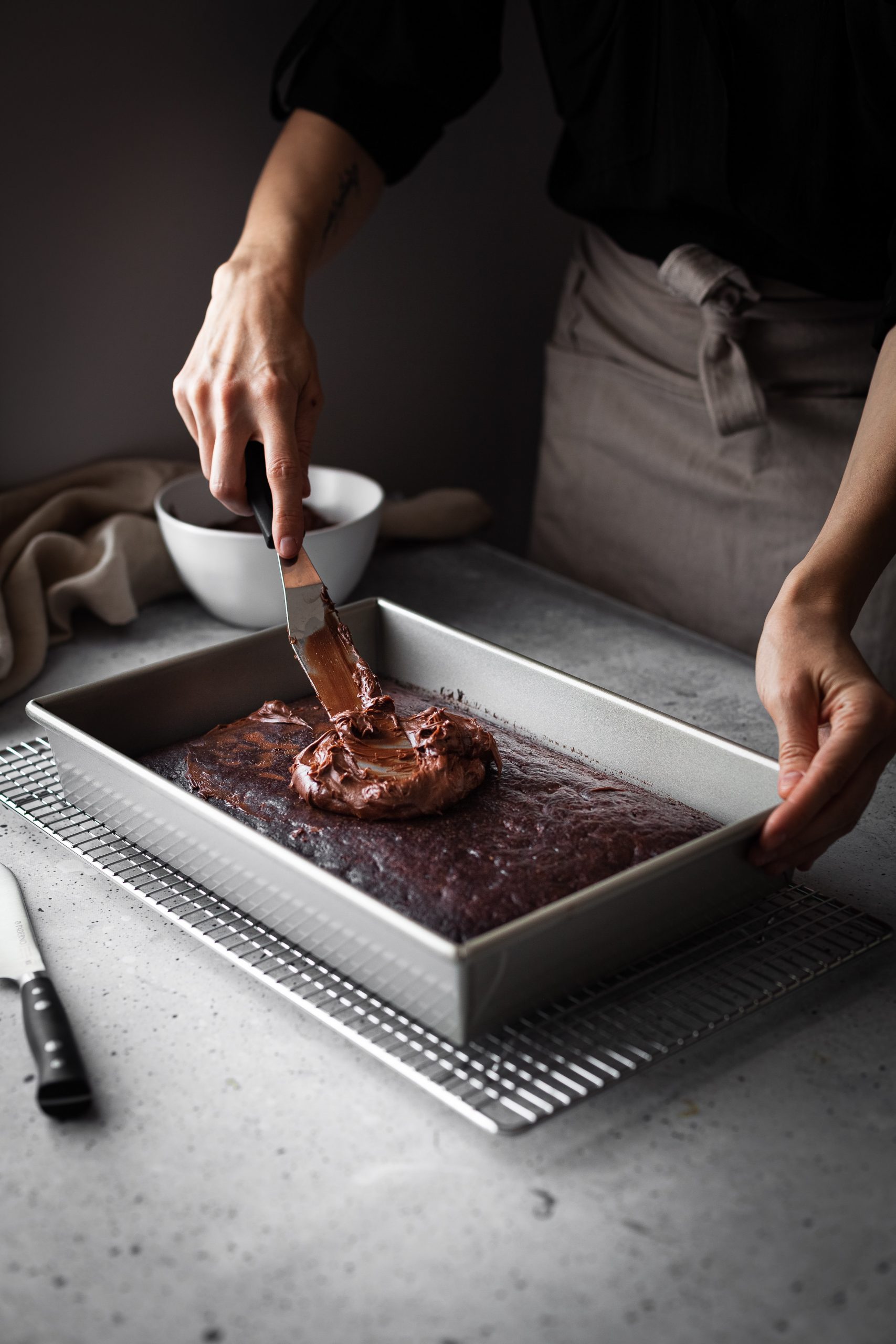 a person spreading chocolate frosting on a cake.