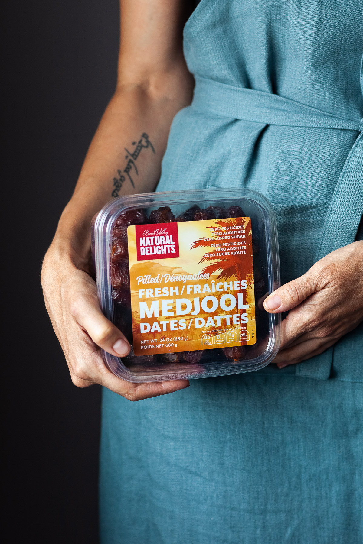 A person in a blue apron holding a box of Medjool dates.