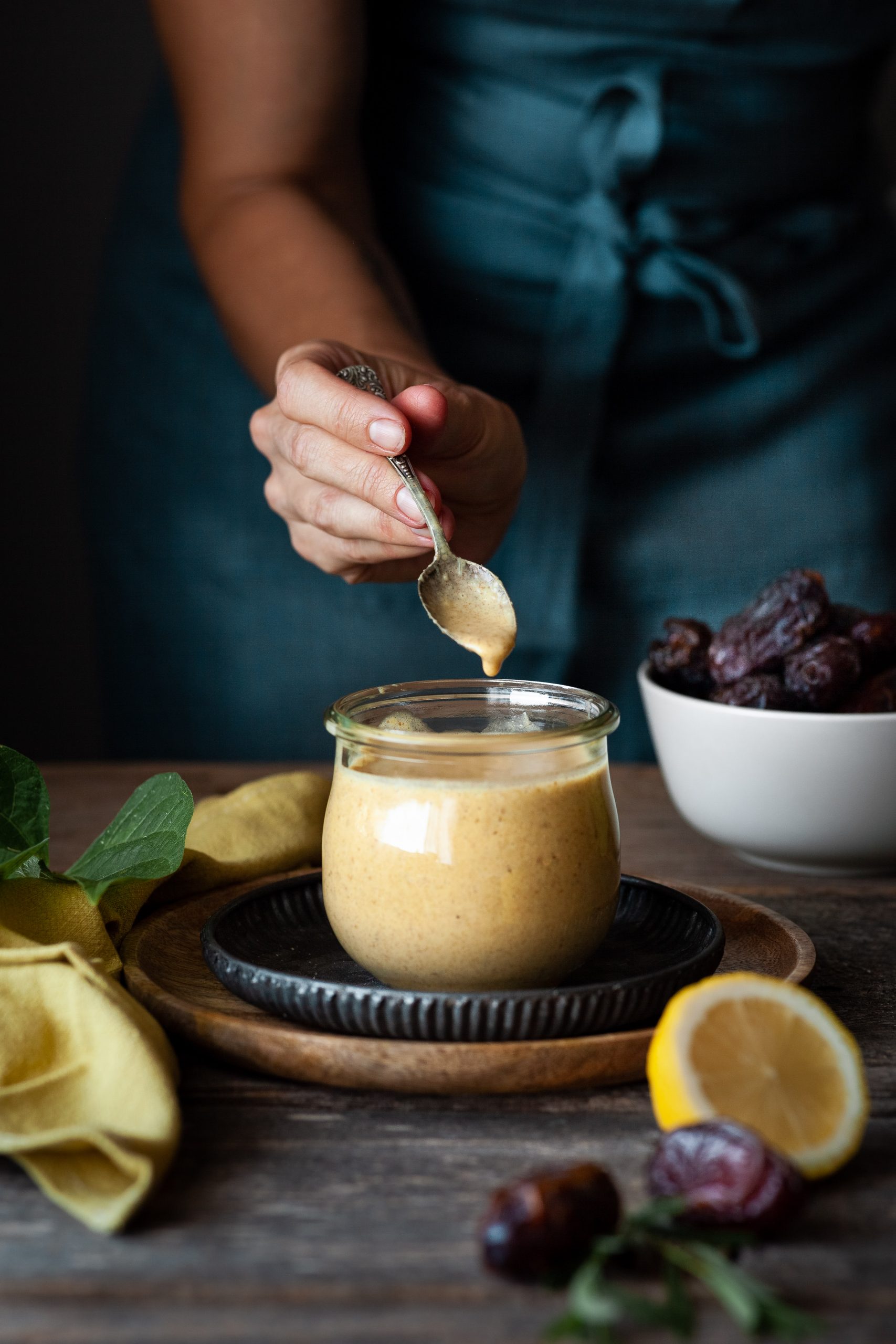 portrait view of a hand dipping a spoon into a bowl of dressing with a yellow linen on the side.
