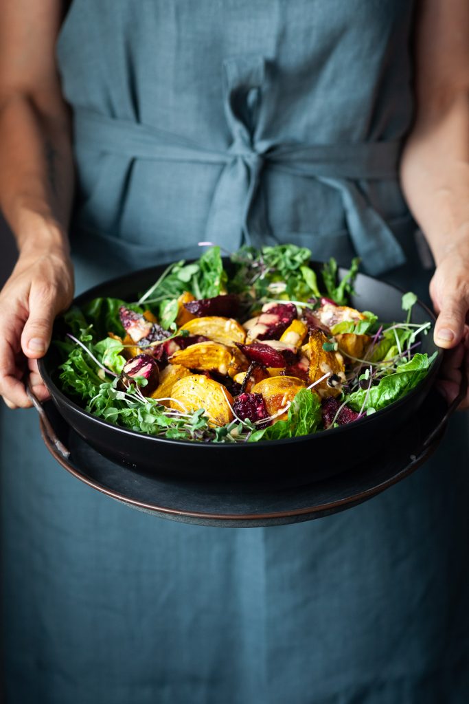 A person in a blue apron holding a bowl of roasted beet salad.
