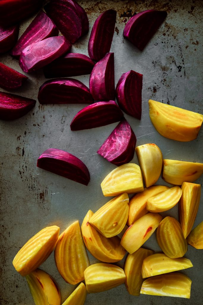 overhead view of sliced purple and gold beet wedges on a baking tray.